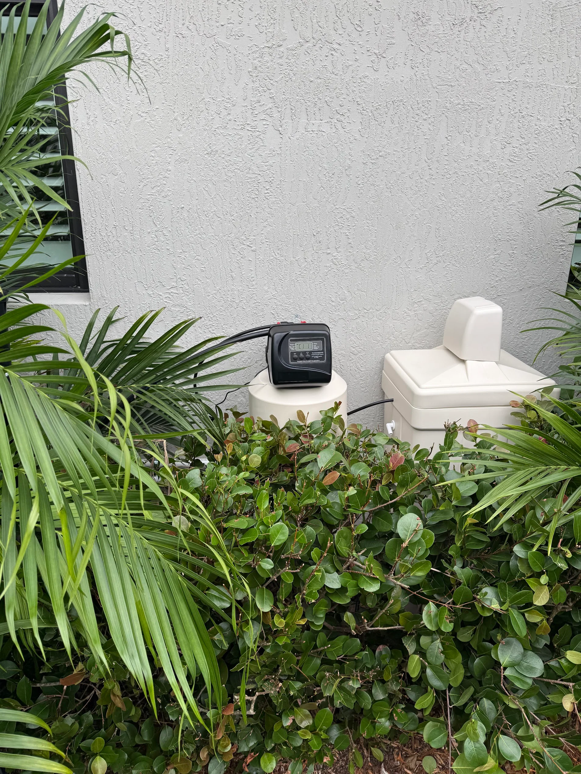 Dual white water softener tanks with digital control head mounted on exterior stucco wall