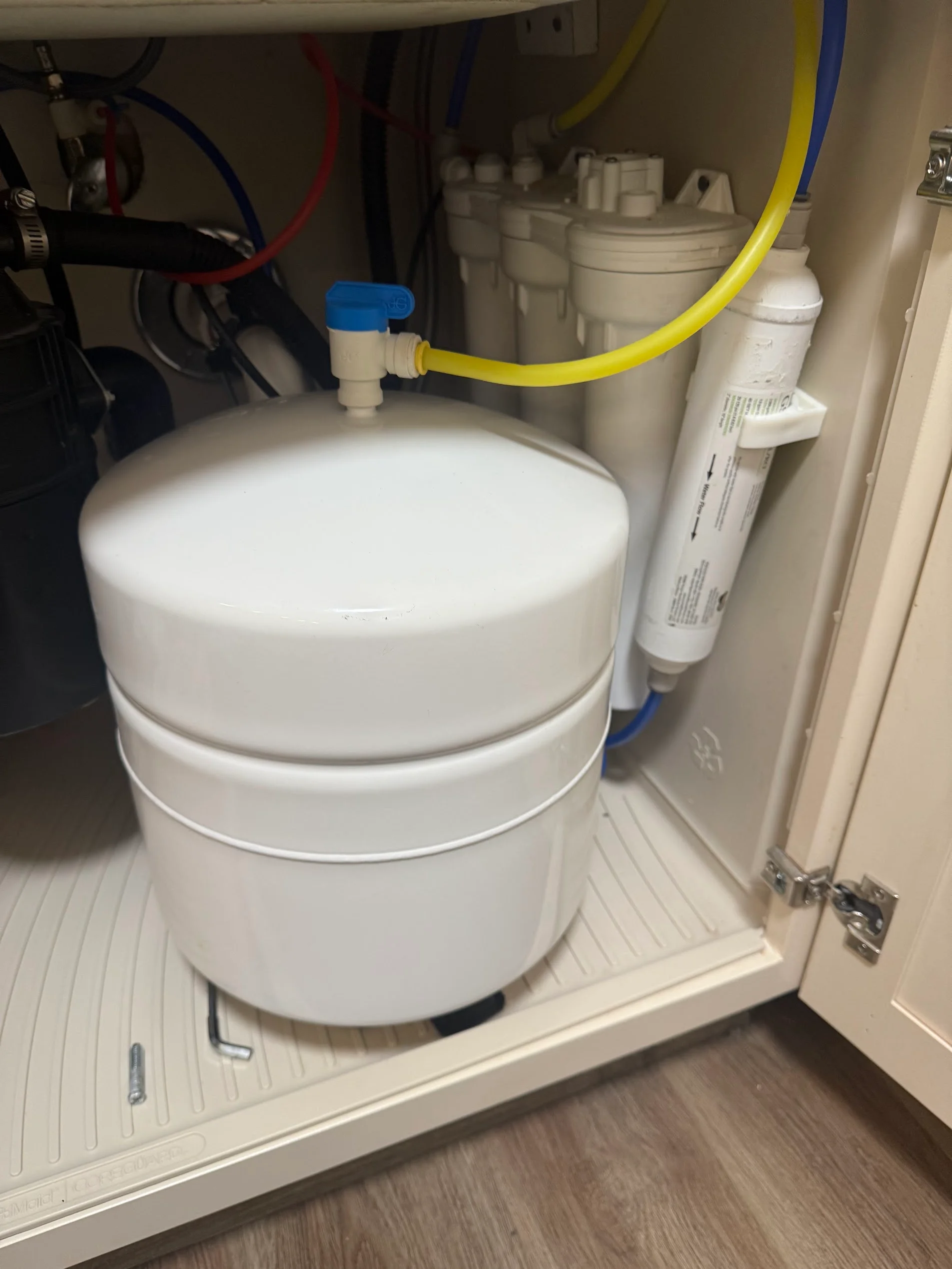 Under-sink reverse osmosis system with white storage tank, filter cartridge, and color-coded supply lines installed in cabinet