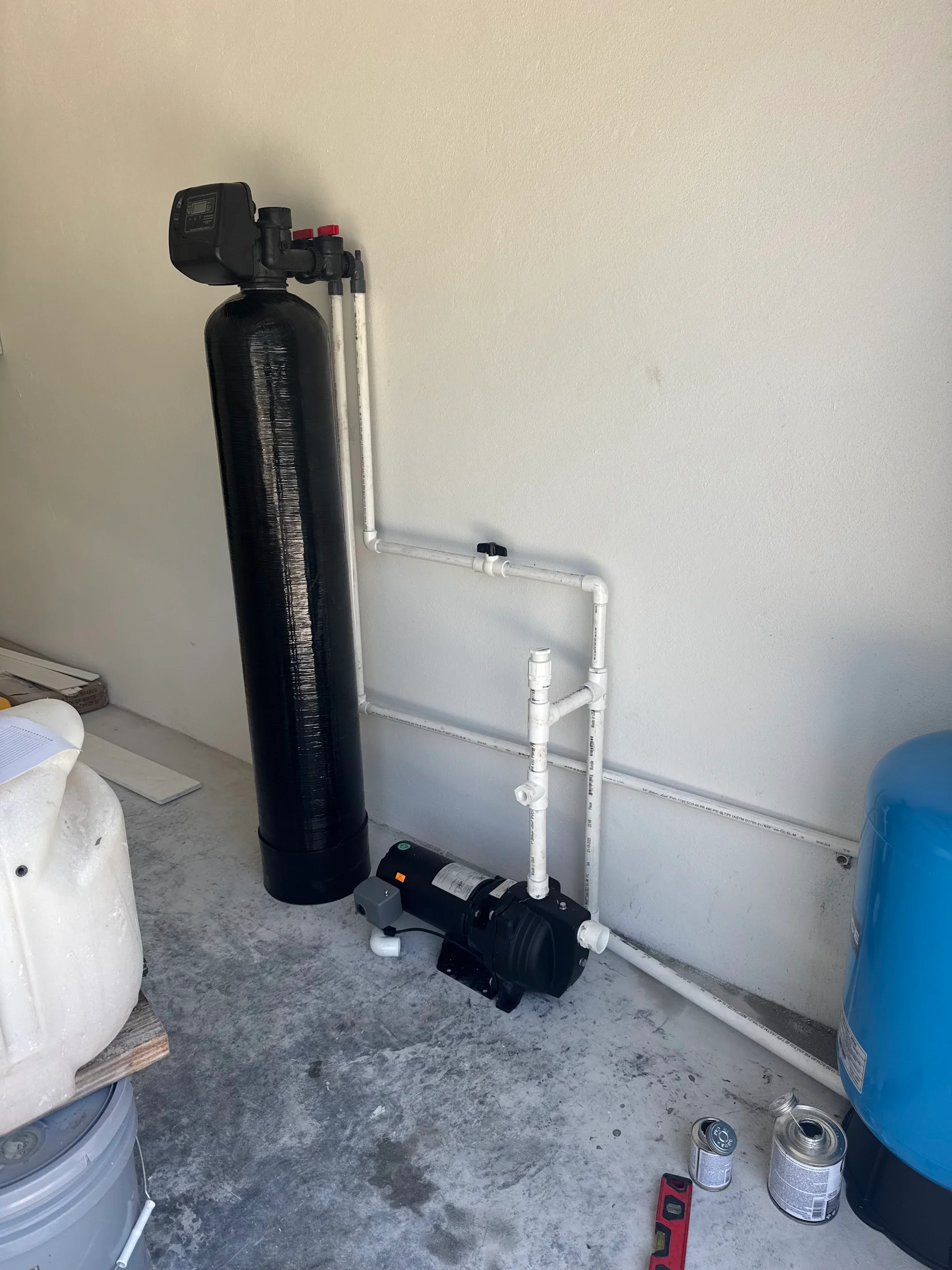 Black water softener tank with automatic valve, white PVC piping, and brine tank installation